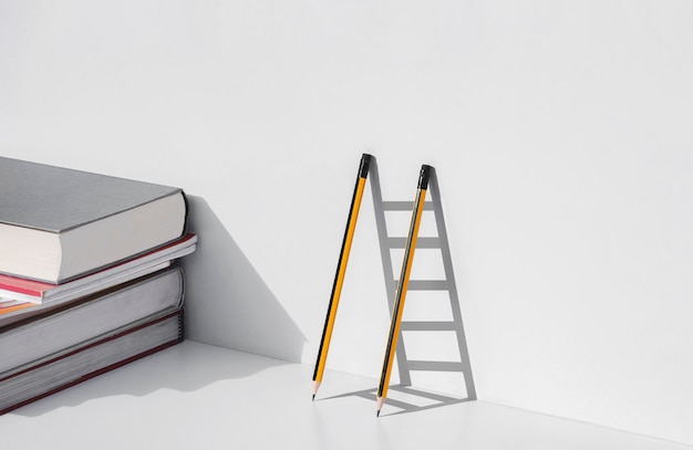 Deux crayons et ombre en forme d'échelle avec pile de manuels sur table blanche