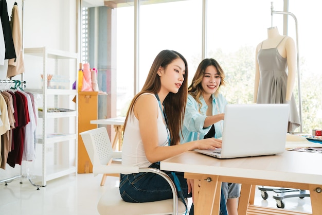 Deux créatrices de mode ou couturières asiatiques ont réfléchi et discuté de la conception de la nouvelle collection avec des exemples de tissus et des croquis sur l'ordinateur portable Travailler ensemble dans le studio