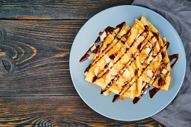 Deux crêpes au sirop de chocolat, flocons d&#39;amandes sur une assiette, miel