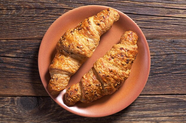 Deux croissants aux graines de sésame dans une assiette sur la vue de dessus de fond en bois foncé