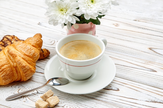 Deux croissants frais et café, fleurs sur fond de bois