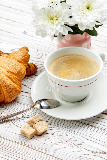 Deux croissants frais et café, fleurs sur fond de bois