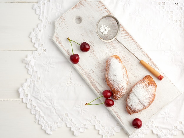 Deux croissants frais saupoudrés de sucre glace sur une planche en bois blanche