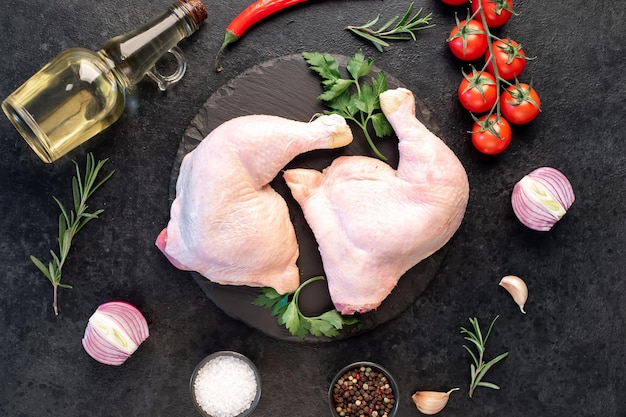 deux cuisses de poulet crues avec des épices et des herbes sur un fond de pierre