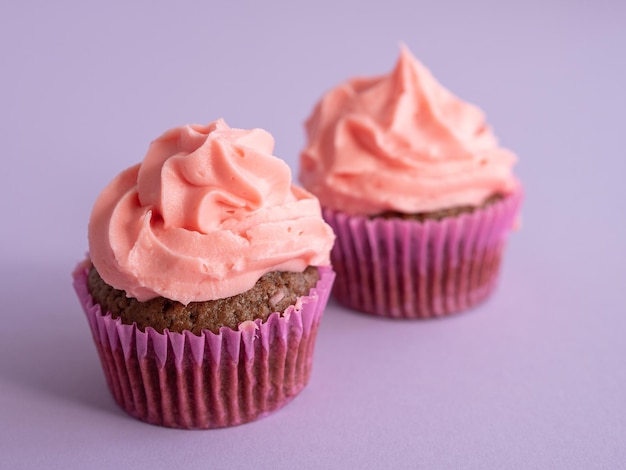 Deux cupcakes sur fond violet avec un bonnet de crème rose