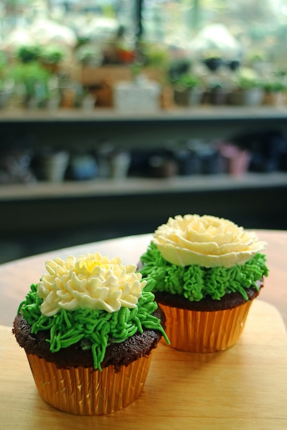 Deux cupcakes garnis de crème fouettée en forme de fleur servis sur une table en bois