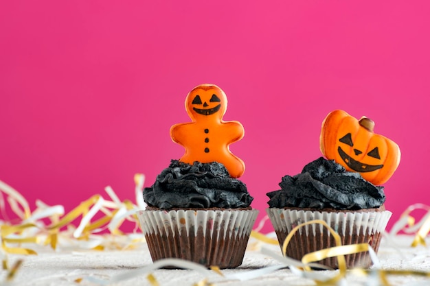 Deux cupcakes pour la célébration d'Halloween sur fond rose Cupcake d'Halloween avec des citrouilles et un bonhomme en pain d'épice