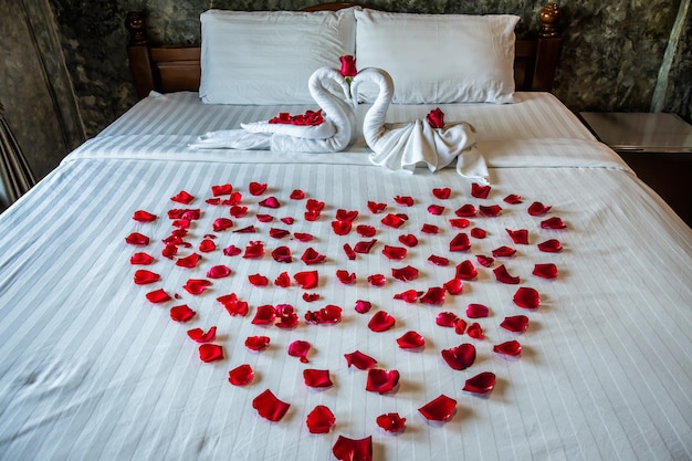 Photo deux cygnes sur le lit roulé de serviettes sur un lit blanc avec des roses rouges disposées en forme de cœur décorations spéciales pour la lune de miel et le jour de la saint-valentin à l'hôtel