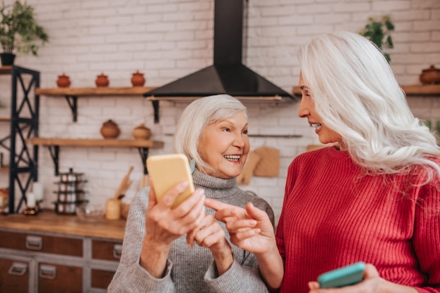 Deux dames positives aux cheveux gris matures parlent de nouvelles technologies