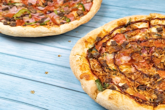 Deux délicieuses grandes pizzas différentes sur un fond en bois bleu.