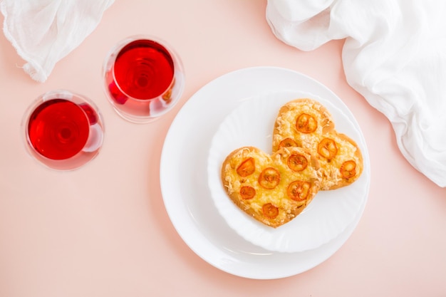 Deux délicieuses pizzas en forme de cœur sur des assiettes et deux verres de vin sur une table dressée pour célébrer la Saint-Valentin. Vue de dessus. Espace de copie