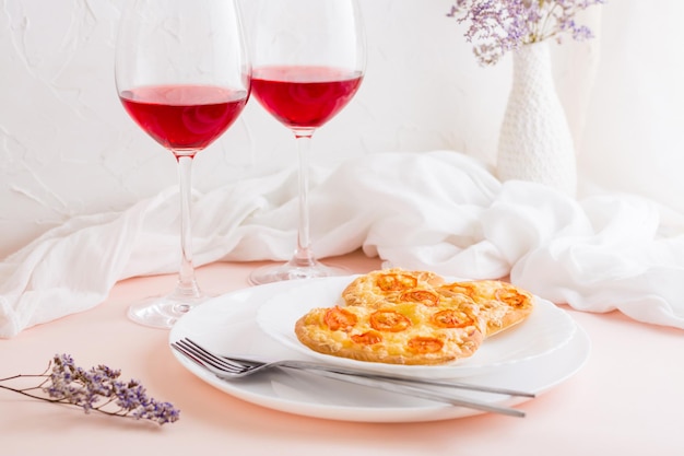 Deux délicieuses pizzas en forme de cœur sur des assiettes et deux verres de vin sur une table dressée pour célébrer la Saint-Valentin