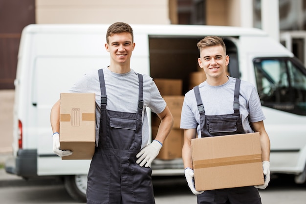 Deux déménageurs en uniforme déchargent la camionnette pleine de cartons Service de déménagement