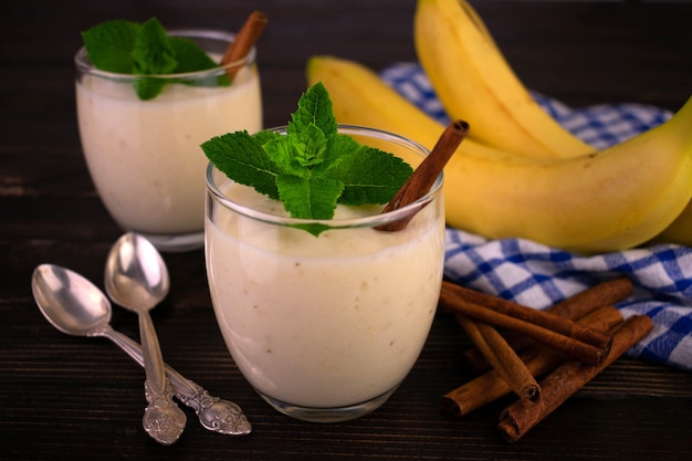 Deux desserts à la banane avec de la cannelle dans des verres sur un fond en bois foncé.