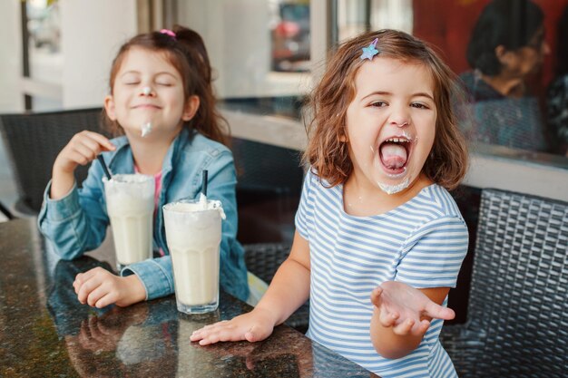 Photo deux drôles de petites sœurs caucasiennes, des frères et sœurs, boivent des milk-shakes dans un café, des amies, des filles qui s'amusent.