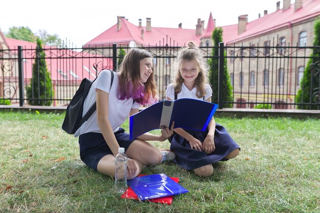 Deux écolières assis sur l'herbe avec des livres près du bâtiment de l'école, filles sœurs