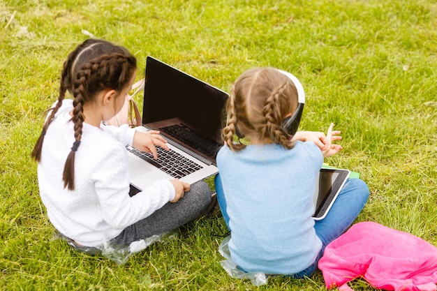 deux écolières drôles s'assoient sur l'herbe et lisent des livres. Les filles, les copines, les sœurs suivent des cours dans la nature.