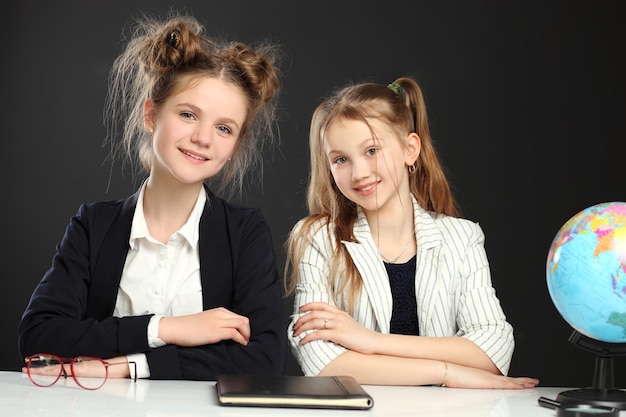 Deux écolières drôles en uniforme scolaire sont assises sur le fond d'un bureau avec des livres