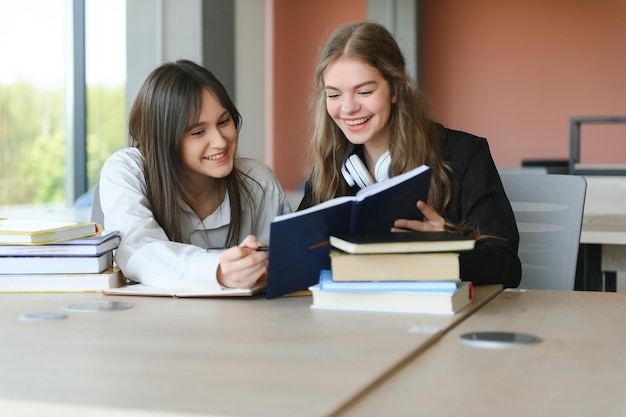 Deux écolières de quinze ans lisant des livres et prenant des résumés dans des cahiers font leurs devoirs à la bibliothèque de l'école