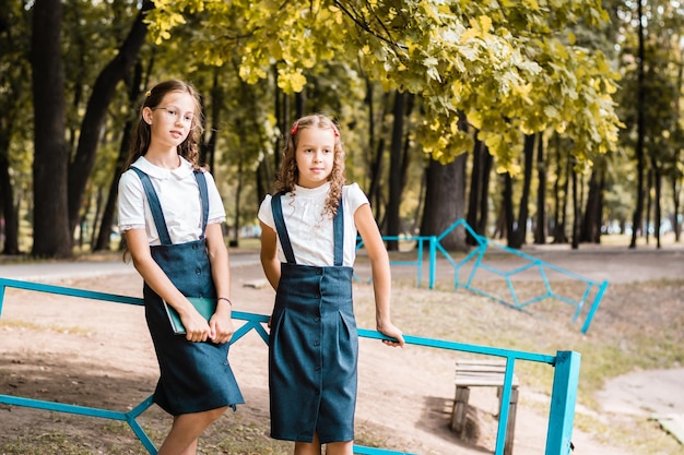 Deux élèves en uniforme scolaire se tiennent près de la clôture dans le parc par une chaude journée