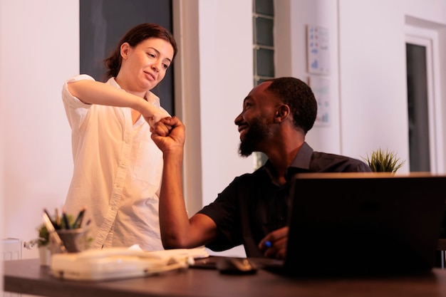 Deux employés divers se cognant les poings, célébrant le résultat d'un travail d'équipe réussi, des collègues heureux travaillant ensemble sur un projet. Des collègues vérifient la recherche marketing de l'entreprise dans un espace de coworking