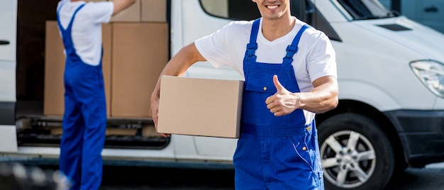 Deux employés d'une entreprise de déménagement déchargent des cartons d'un minibus dans une nouvelle maison