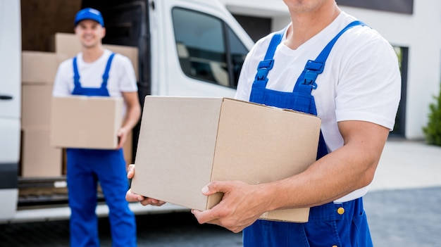 Deux employés d'une entreprise de déménagement déchargent des cartons d'un minibus dans une nouvelle maison