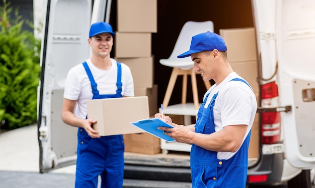 Deux employés d'une entreprise de déménagement déchargent des cartons d'un minibus dans une nouvelle maison