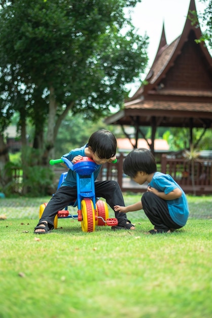 Deux enfants asiatiques jouent et poussent joyeusement des vélos dans le jardin du quartier