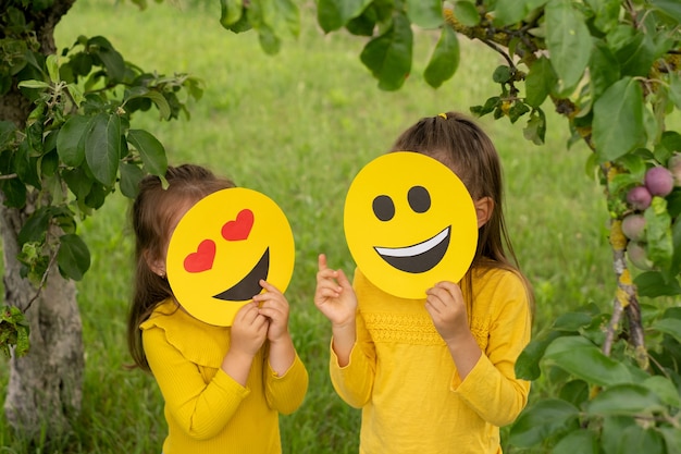 Deux enfants dans le parc se tiennent le visage couvert d'émoticônes heureuses