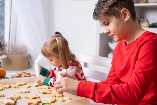 deux enfants frère et soeur en pyjama faisant cuire du pain d'épice festif dans une cuisine décorée de noël