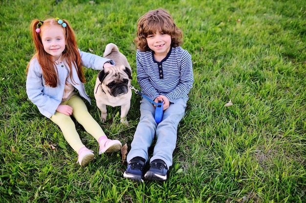 Deux enfants garçon et fille jouant dans le parc sur l&#39;herbe avec chien de race carlin.