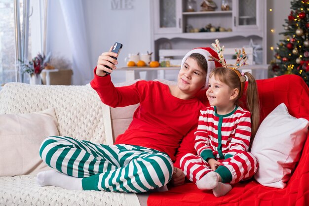 deux enfants garçon et fille en pyjama de Noël confortable utilisant le téléphone, ayant une conversation vidéo avec la famille