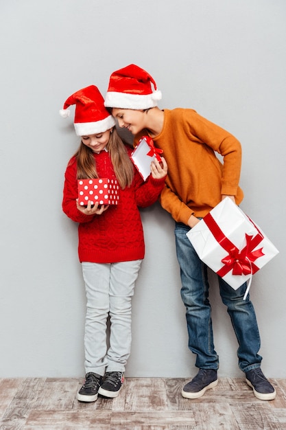 Deux enfants heureux en chapeaux de père Noël debout et regardant à l'intérieur de la boîte-cadeau