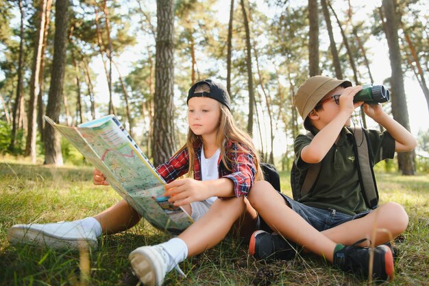 Deux enfants heureux s'amusant lors d'une randonnée en forêt par une belle journée dans une forêt de pins Joli garçon scout avec des jumelles lors d'une randonnée dans la forêt d'été Concepts de scoutisme d'aventure et de tourisme de randonnée