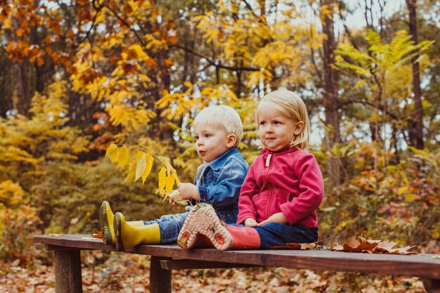 Deux enfants heureux souriants amis, garçon et fille assis sur le banc dans le parc sous les arbres d'automne