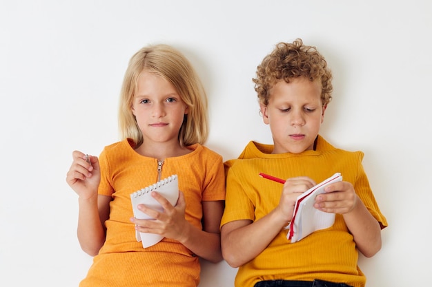 Deux enfants joyeux se trouvent sur le sol avec des blocs-notes et des crayons mode de vie d'enfance inchangé