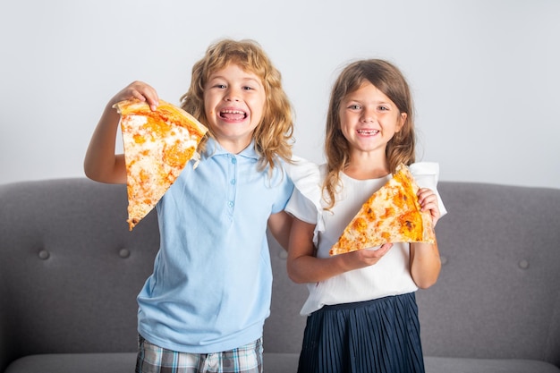 Deux enfants mangeant de la pizza et souriant à l'intérieur heureux enfants souriants tenant une tranche de pizza près du visage