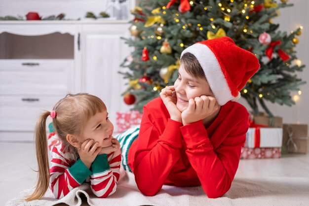 Deux enfants en pyjama de Noël avec des coffrets cadeaux sous l'arbre de Noël à la maison