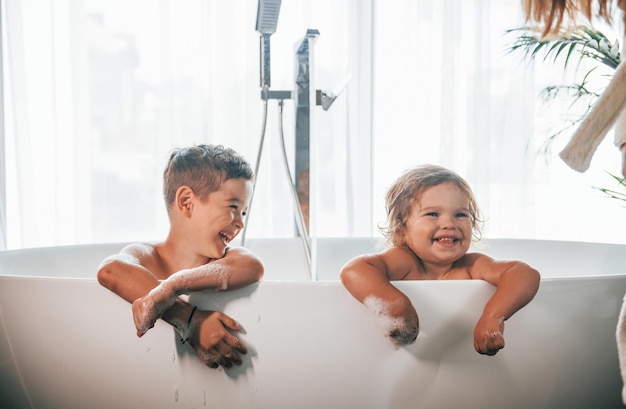 Deux enfants s'amusant et se lavant dans le bain à la maison Posant pour un appareil photo