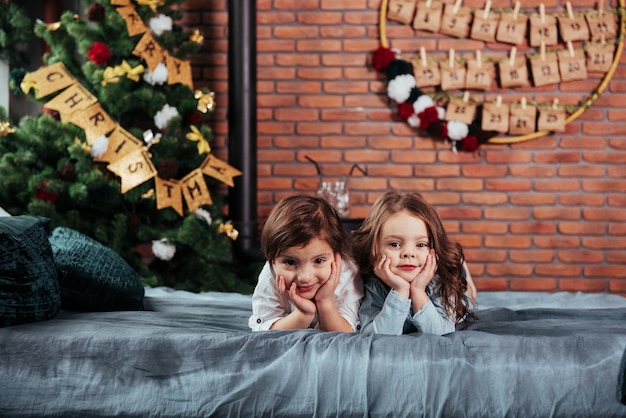 Deux enfants de sexe féminin joyeux allongés sur le lit avec des décorations du nouvel an et un arbre de vacances.