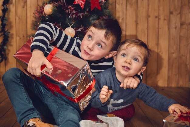 Deux enfants surpris en train de jouer dans la chambre avec leurs cadeaux de Noël sur un fond en bois