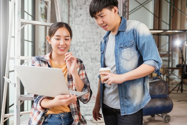 Deux entrepreneurs intérieurs asiatiques masculins et féminins consultent et examinent la rénovation de la maison sur le site avec un ordinateur portable et un dessin sur papier, un ingénieur et un concepteur asiatiques expliquent et discutent sur le site de construction