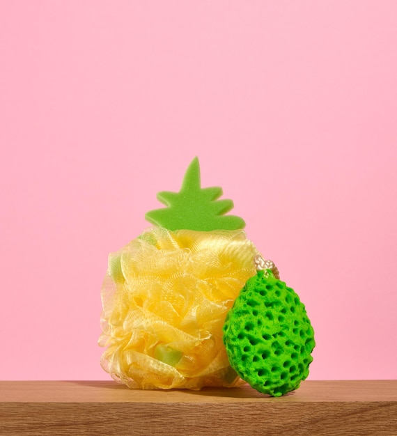 Deux éponges de douche sur une table en bois Une éponge en forme d'ananas mûr jaune Fournitures hygiéniques lumineuses pour la salle de bain