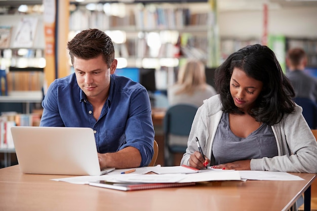 Deux étudiants adultes travaillant sur ordinateur portable dans la bibliothèque du Collège