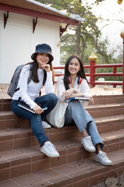 Deux étudiants asiatiques heureux assis dans les escaliers du campus universitaire et souriant à la caméra.