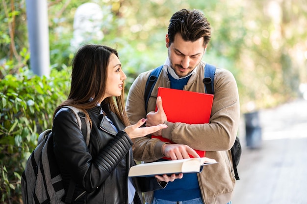 Deux étudiants, hommes et femmes, discutant à l'extérieur, tenant des livres