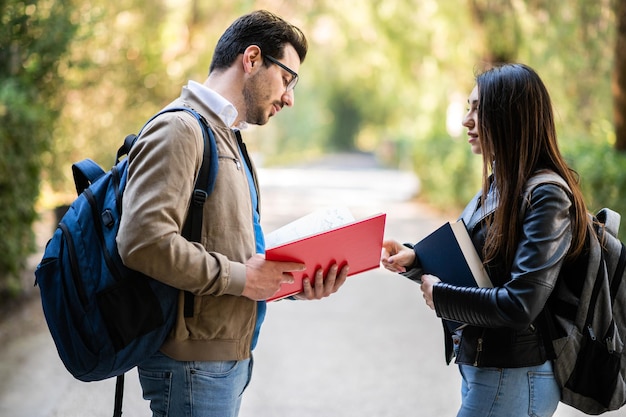 Deux étudiants, hommes et femmes, discutant à l'extérieur, tenant des livres