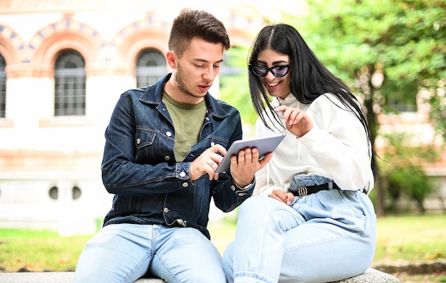 Deux étudiants qui étudient avec une tablette numérique assis sur un banc en plein air
