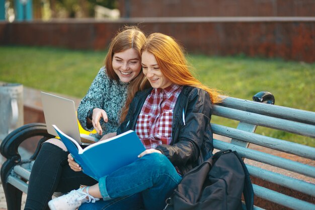 Deux étudiants, s'asseoir banc, regarder livre, et, sourire